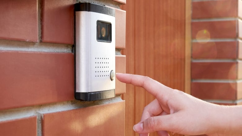 A closeup of a woman's hand about to press a button on a doorbell with a camera and an intercom.