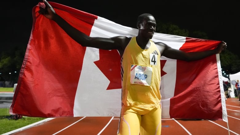 A track and field athlete is seen posing for a picture with the Canadian flag behind his arms.