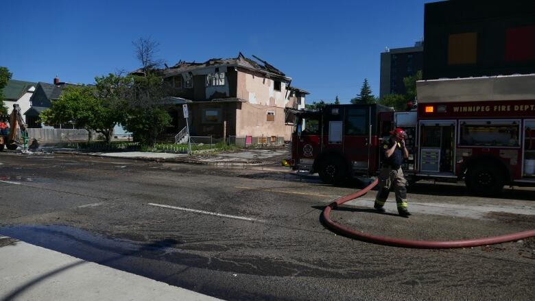 A firefighter stands next to a firetruck in front of a home that was previously on fire. 