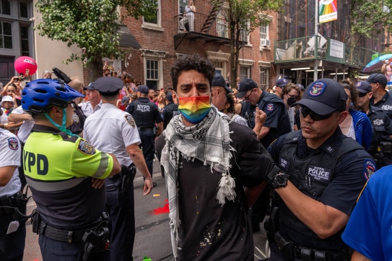 A person wearing a rainbow-coloured face mask is detained by police.