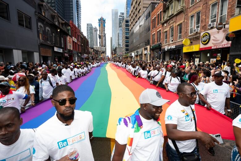 Marchers carry a large rainbow flag down a street.