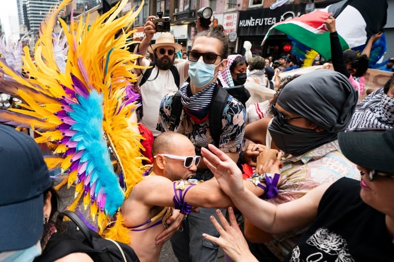 A person wearing a costume pushes protesters with their faces covered.