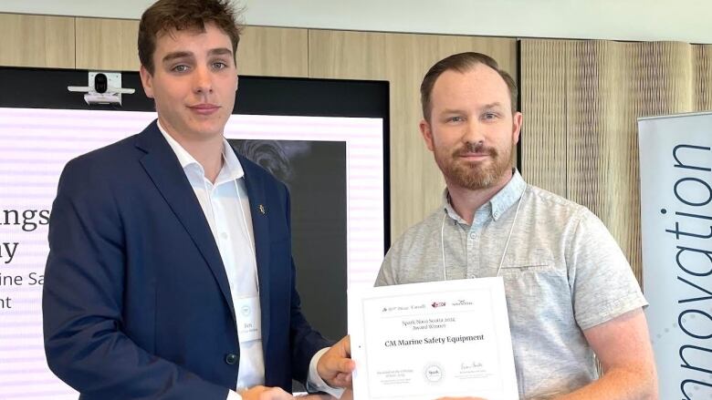 A young man in a blue sports jacket accepts a certificate from an older man. 