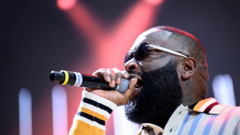 A Black man sings into a microphone at a concert.