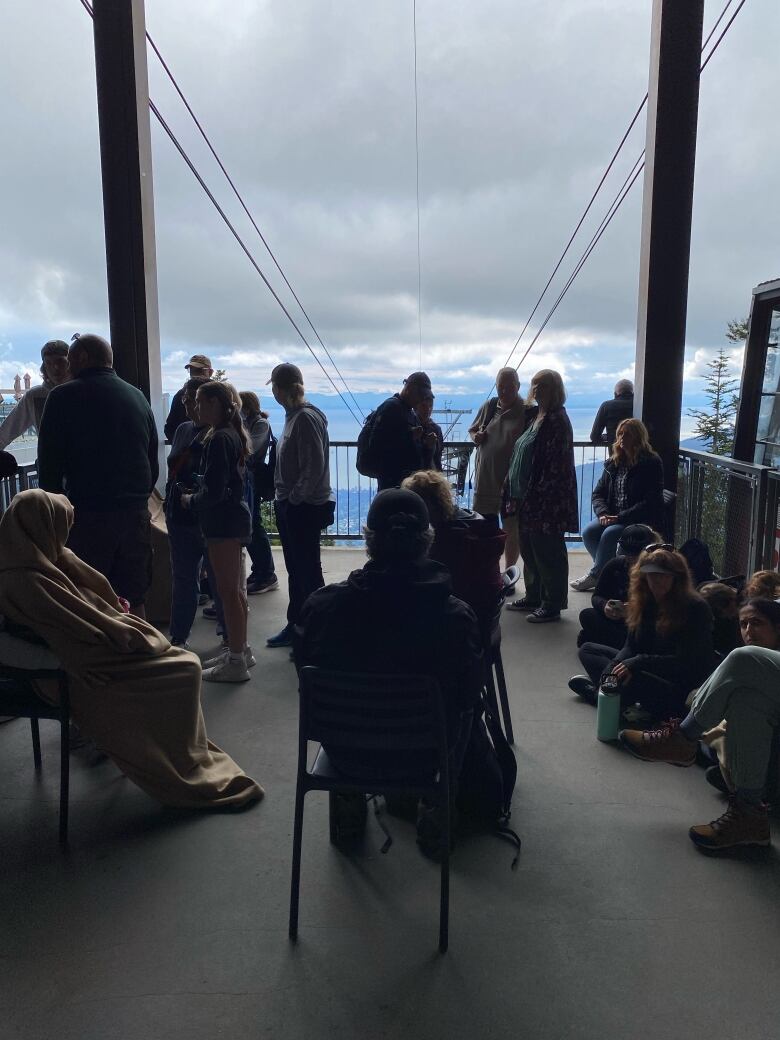 People wait on a platform, with skychair-like lift lines visible in the background.