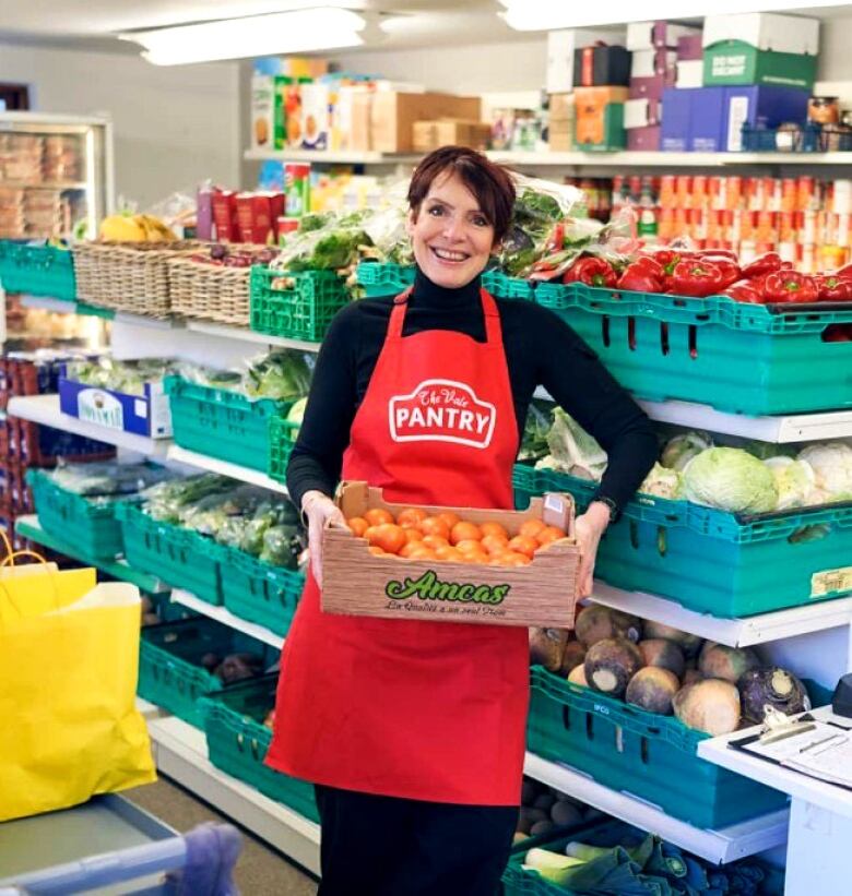 A woman stands smiling with a basket in a store.