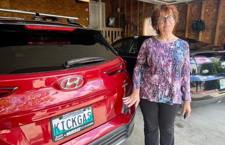 A woman standing next to a car in a garage.