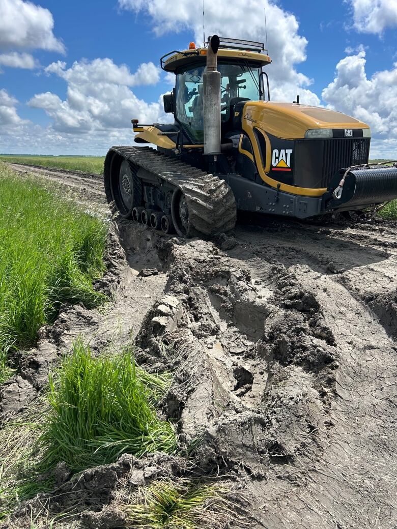 A tractor with tracks is pictured on a rutted road.