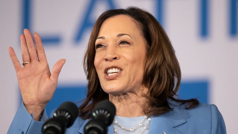 A woman smiles and gestures while speaking into a microphone.