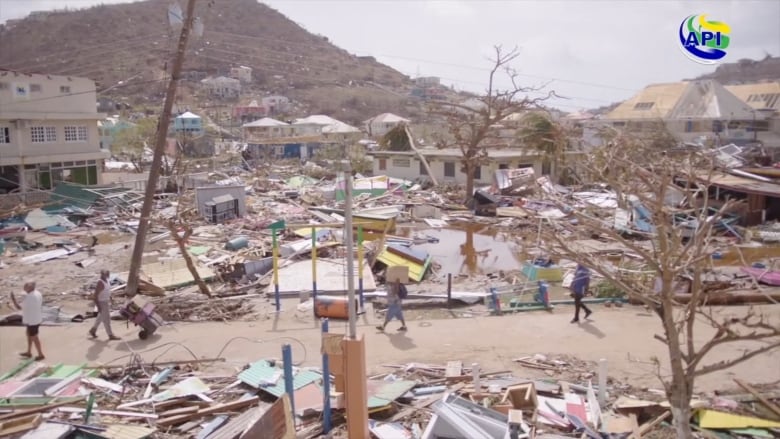 People walk on a road amid homes and properties littered with debris.