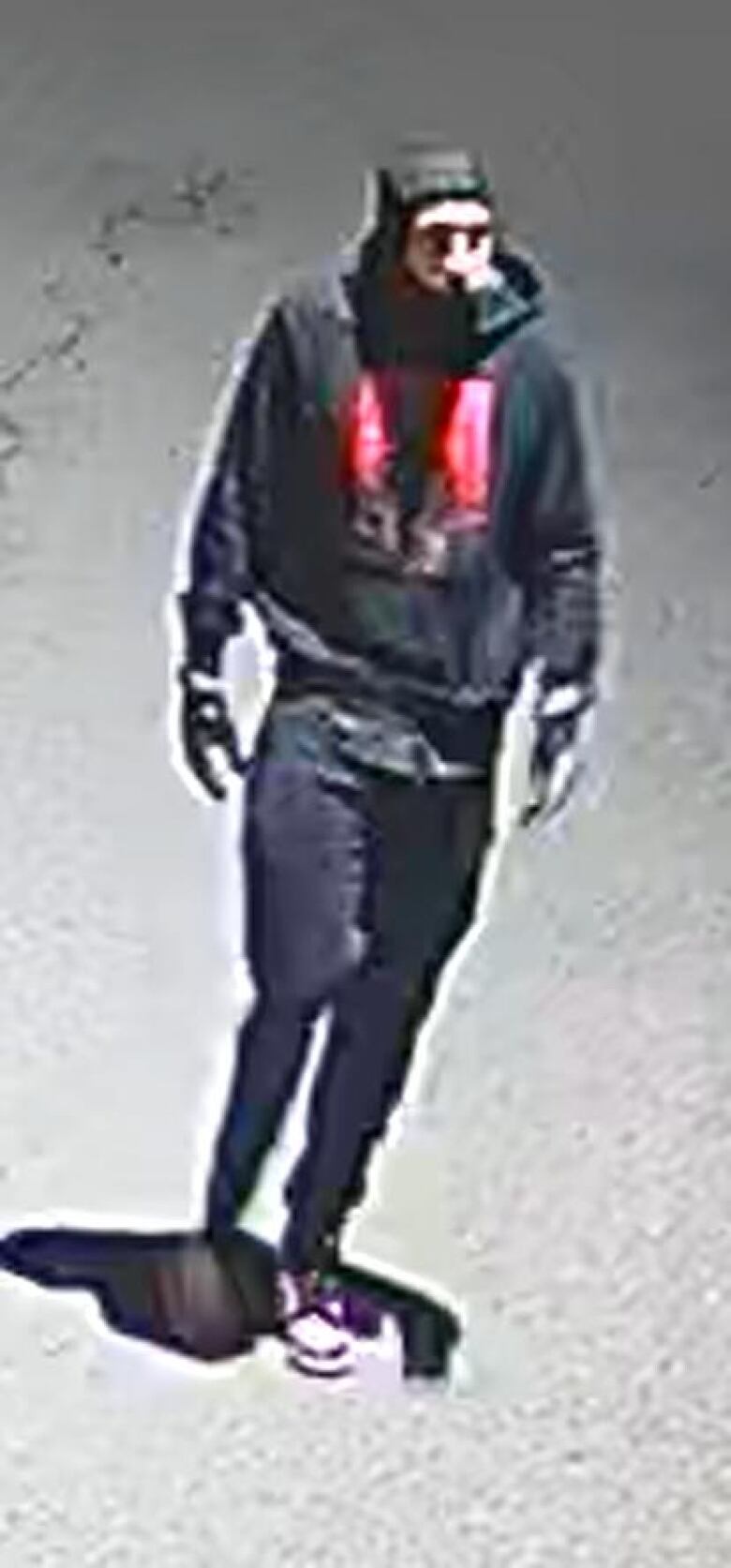 A man in dark clothing, with a red logo on his hoodie. 