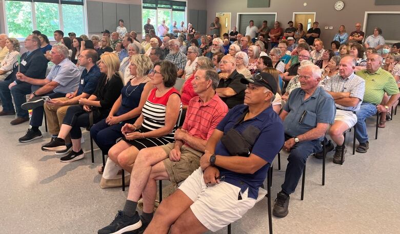 About 80 people sit on chairs in a church hall building. 