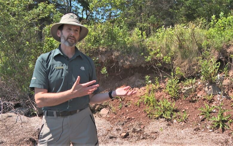 Jesse Francis gestures at a shell midden emerging from a bank.