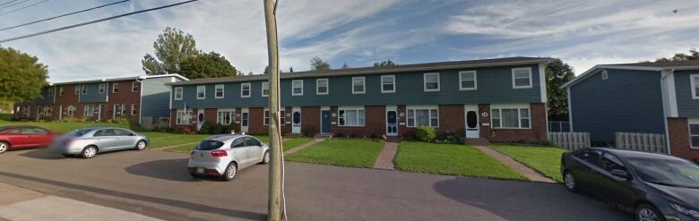 Three long two-storey apartment buildings with some cars parked out front. 