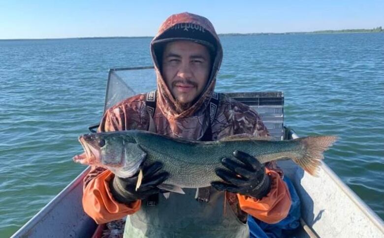 A man standing in a boat holds up a fish.