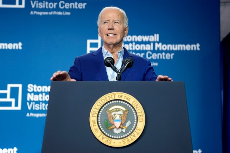 Joe Biden, wearing a navy blue suit, stands behind a blue podium bearing the presidential seal. There is a blue backdrop behind  him with the words 