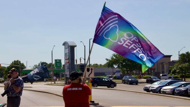 A person waves a tie-dye OPSEU flag in a parking lot.