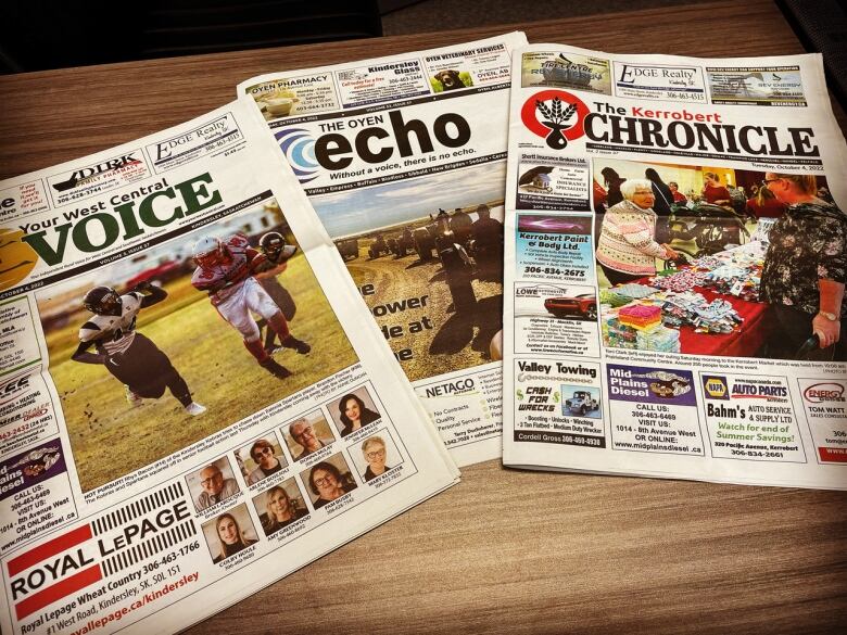 Three papers from Saskatchewan and Alberta are displayed on a table.