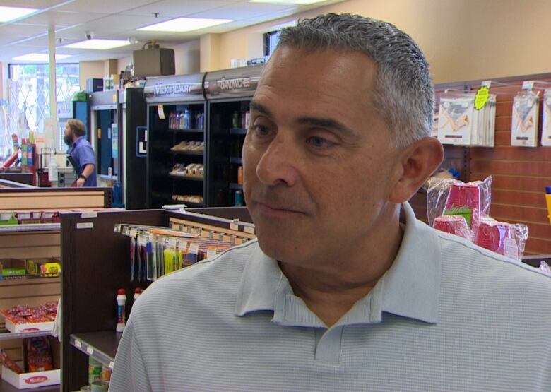 A man wearing a collared T-shirt stands in a convenience store.