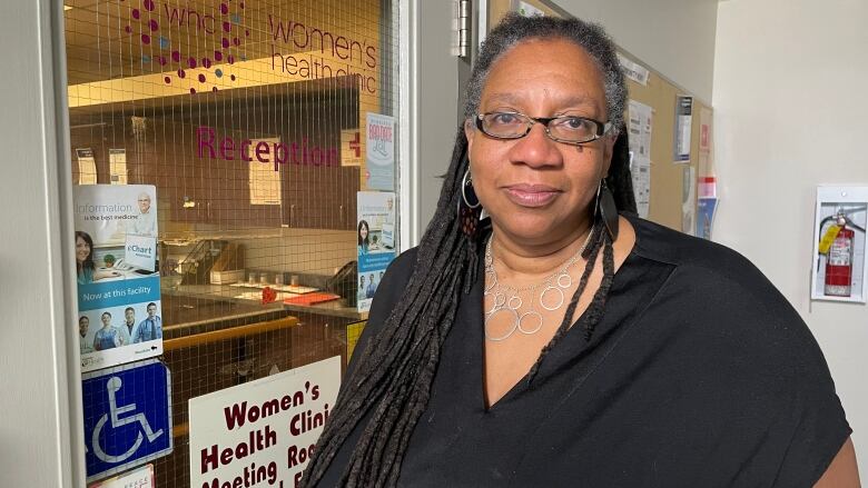 A woman in a black shirt stands in front of the door to the Women's Health Clinic.