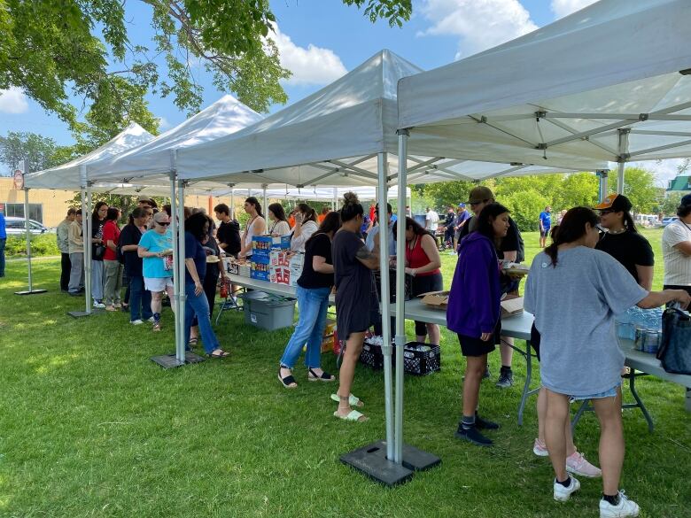 Dozens of people line up under tents to be given food that was cooked on grills