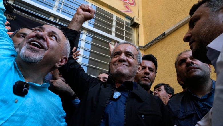 An Iranian politician pumps his fist in the air as people crowd around him.