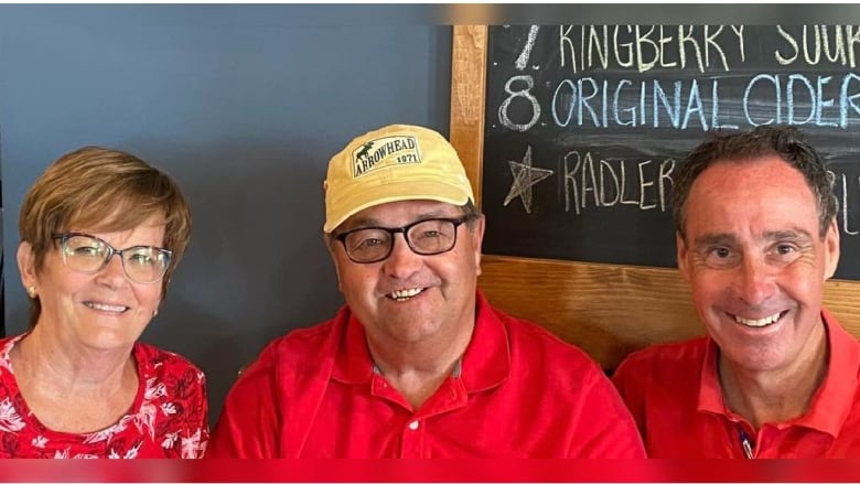 Three people wearing red, sitting at a booth and smiling. 