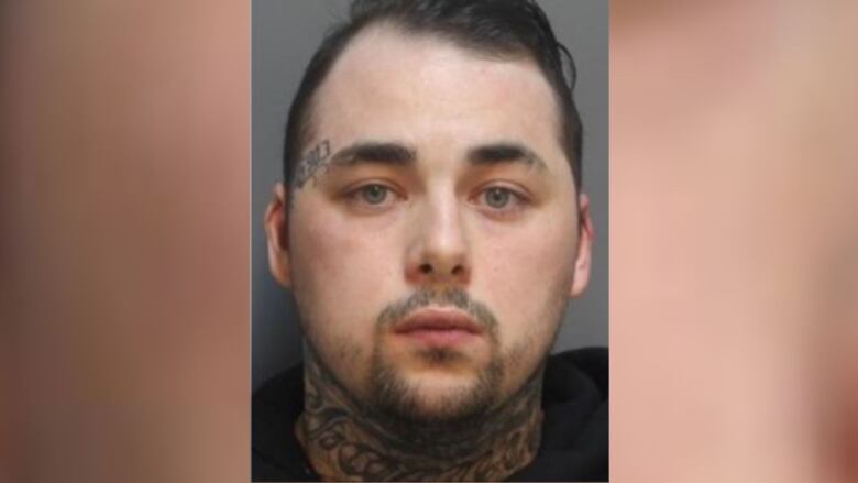 A man with elaborate neck tattoos and a thin french beard is seen in a mugshot.