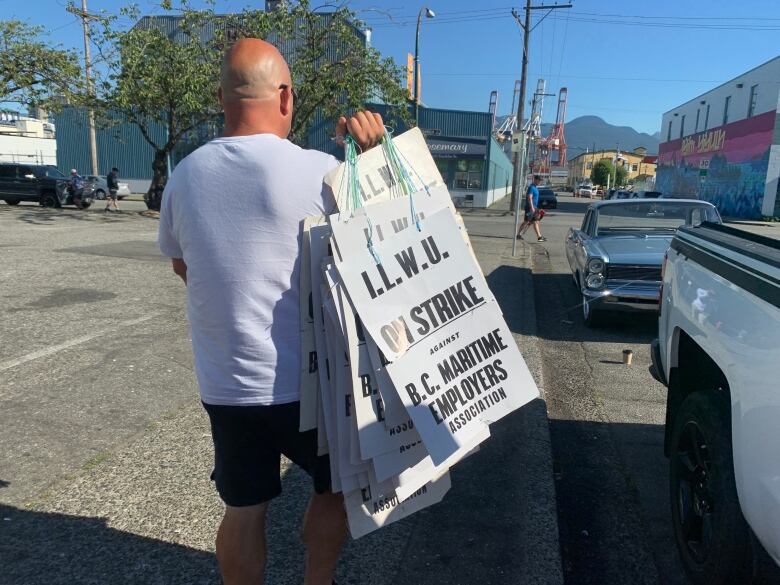 A man holds a series of sandwich boards that read 'I.L.W.U. On Strike against B.C. Maritime Employers Association'.