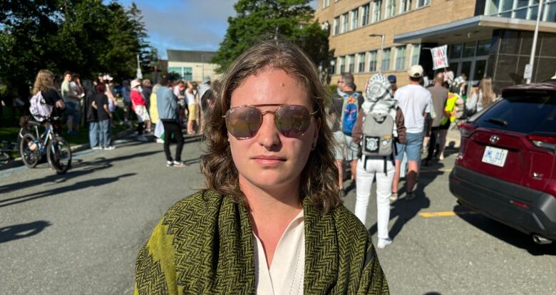 Person with shoulder length hair wearing sunglasses standing in parking lot.