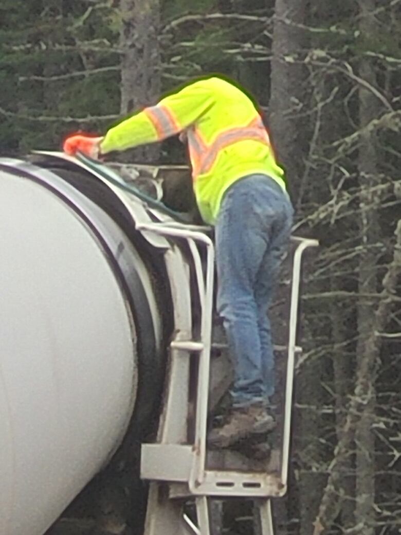 A construction worker standing on a cement roller truck.