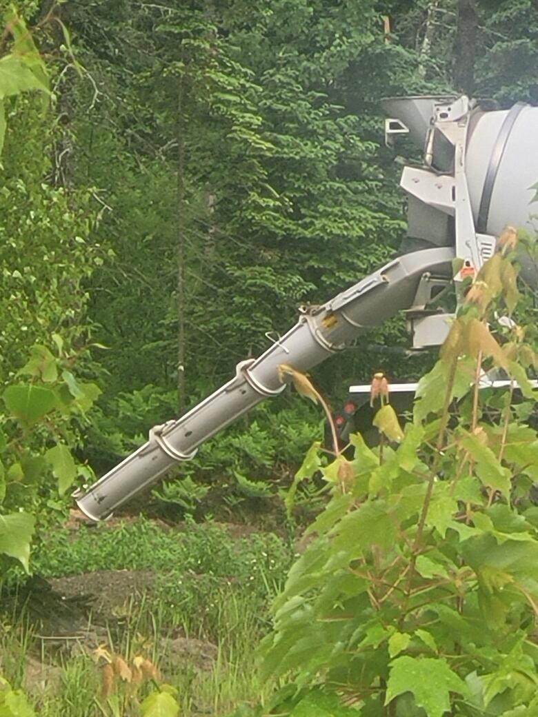 Cement truck with its cement shoot in the woods.