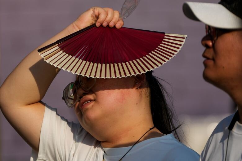 A woman uses a fan as she walks with her companion on a hot day in Beijing in June. June 2024 was the hottest June on record, according to Europe's Copernicus climate service.