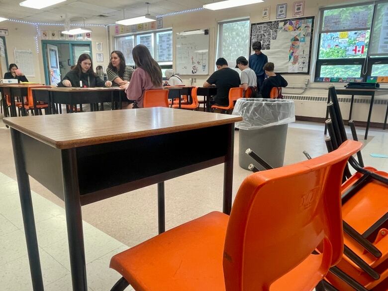 An empty desk is seen with students sitting in other desks in the distance. 