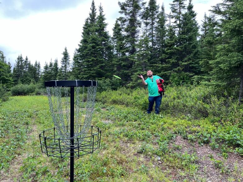 A man fires a frisbee toward a metal basket on a disc golf course.