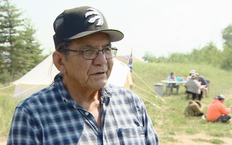 Willie Ermin wearing plaid shirt and Toronto Raptors cap with tent in background