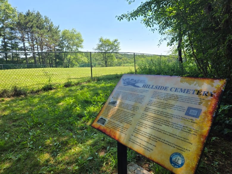 An interpretive sign that reads Hillside Cemetery stands outside a fenced in field.