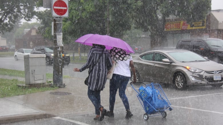 Two women share an umbrella as heavy rains fall.