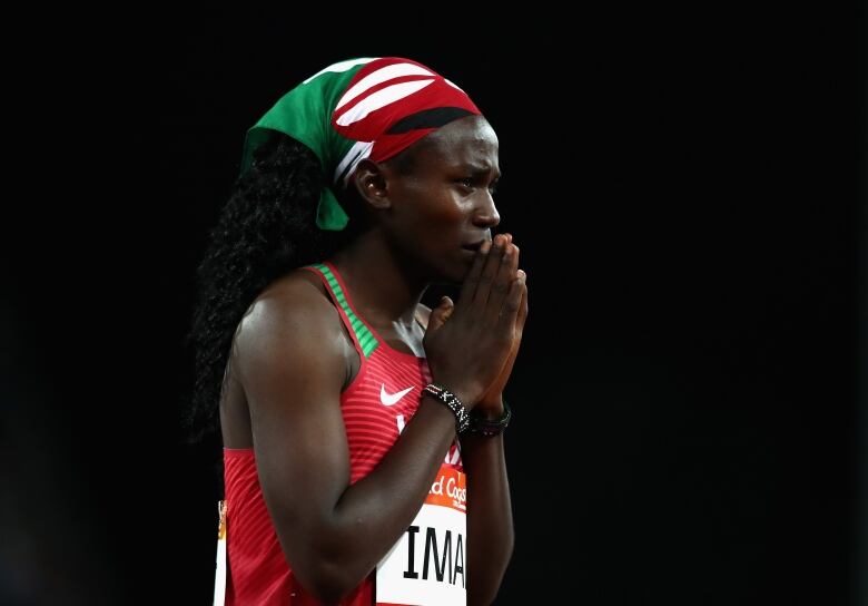 A woman in a red Nike running jersey and a red and green headscarf holds her hands to her face.