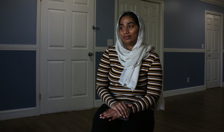 A woman sitting and staring out a window with her hands on her lap.