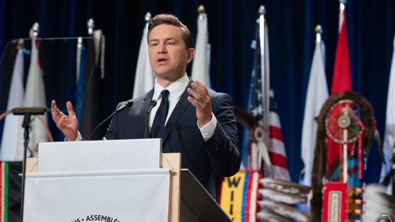 Pierre Poilievre, stands at a podium with his arms outstretched.