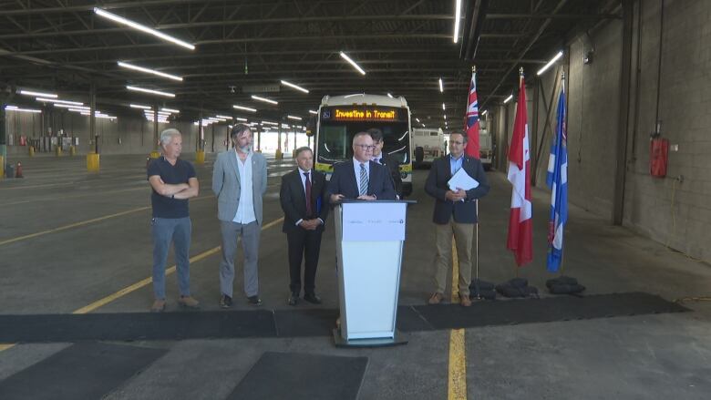 A group of men standing in front of a podium, with a bus that says 