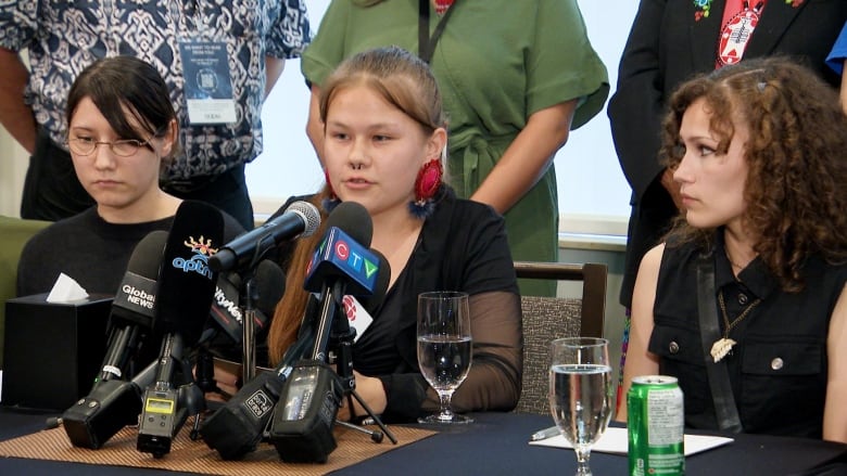 Three women sit at a table that has water glasses in front of them.  