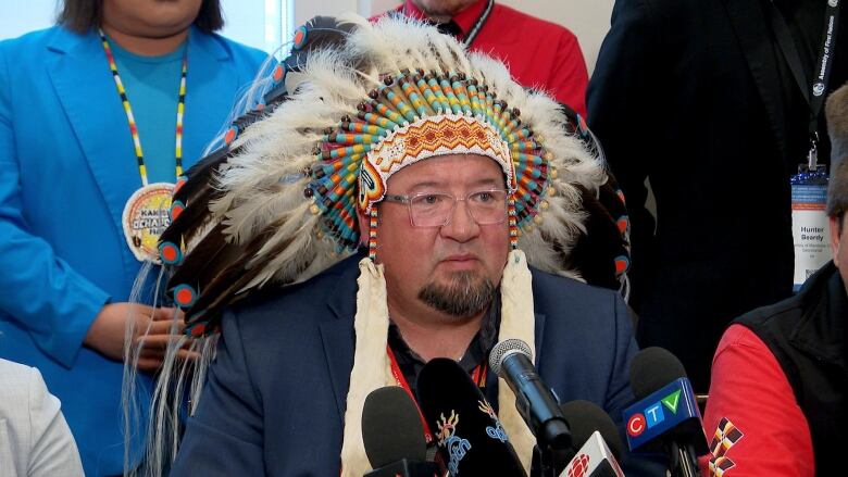 A man wears a First Nations traditional headdress at a press conference. 