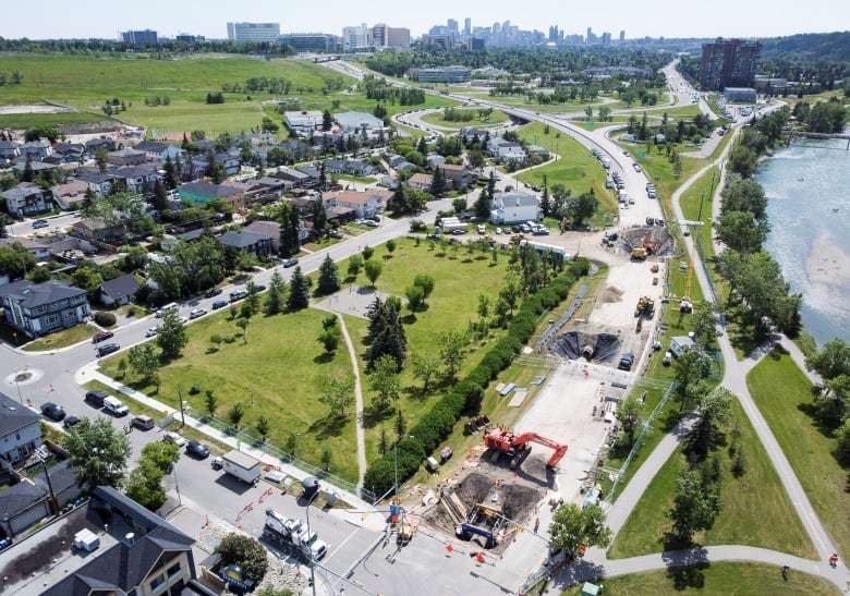 an aerial view of three sections of road with massive construction occurring. the city skyline and river are in the background.