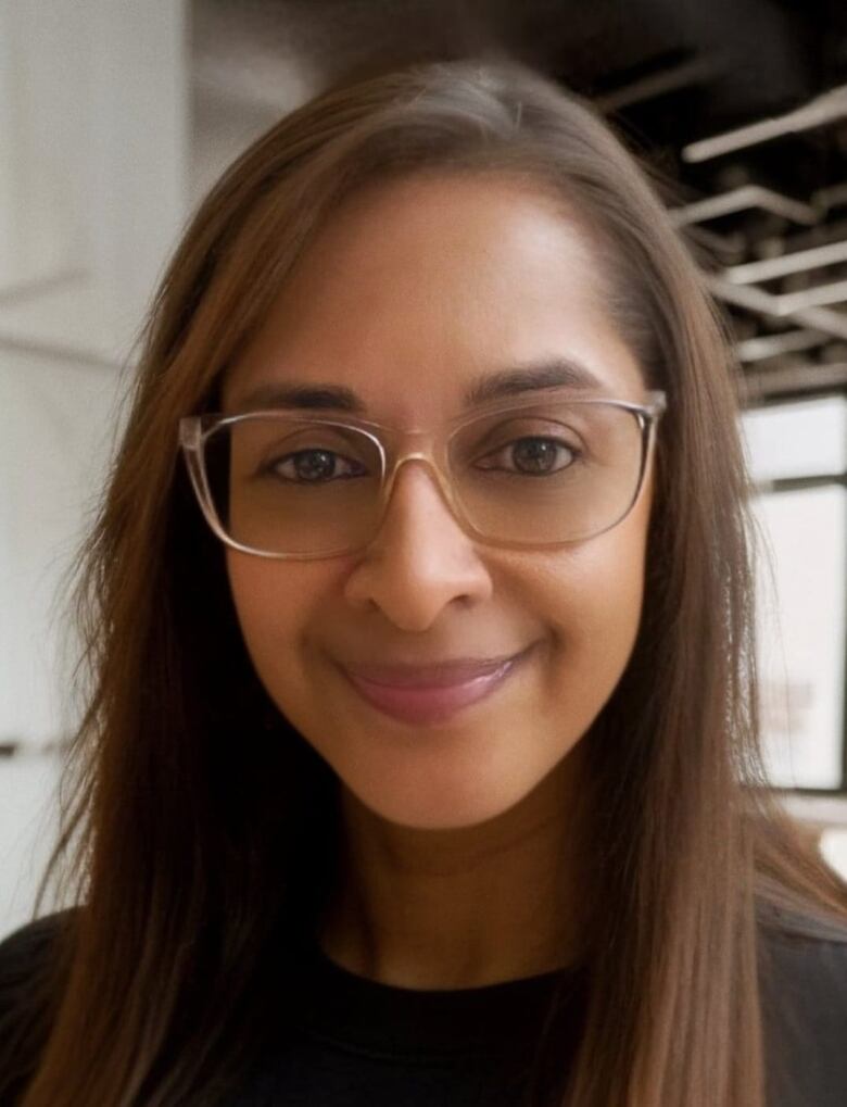 A woman with glasses smiles at the camera