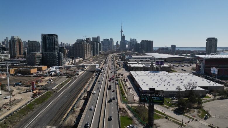 A sunny day in Toronto. An aerial drone view of the Gardiner Expressway, with cars on it, looking toward downtown. The lake is on the right.