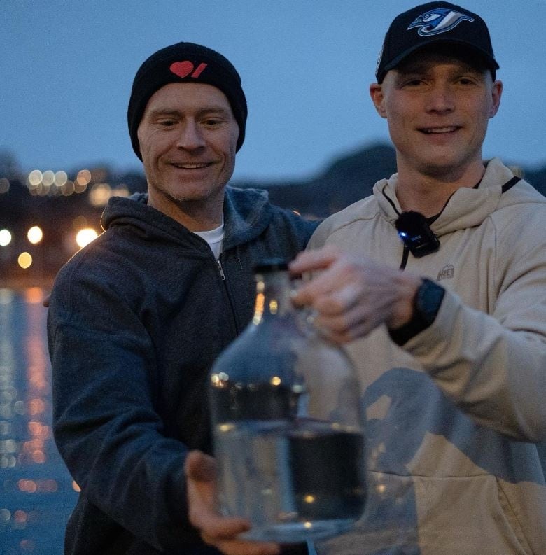 Two men hold up a jug of water.