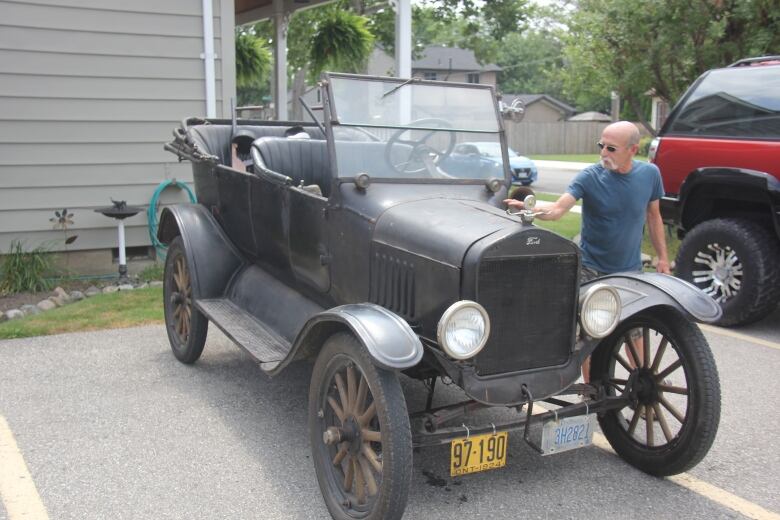 A man stands to the right of a very old black car