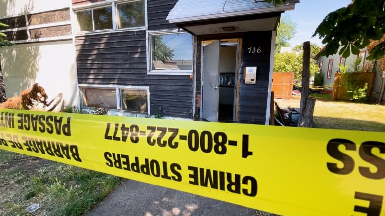 Yellow crime tape blocks off access to an apartment building, which has visible smoke damage on it.